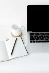 imagem de uma mesa com laptop, agenda com caneta e uma xícara de café